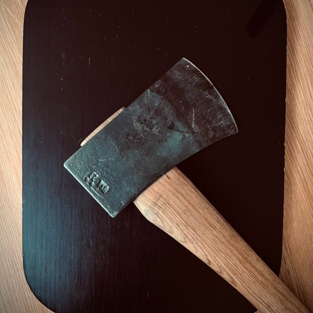 A Council Tool Boy’s Axe with a wooden handle resting on a dark wood surface, representing heirloom quality tools built for a lifetime of use.