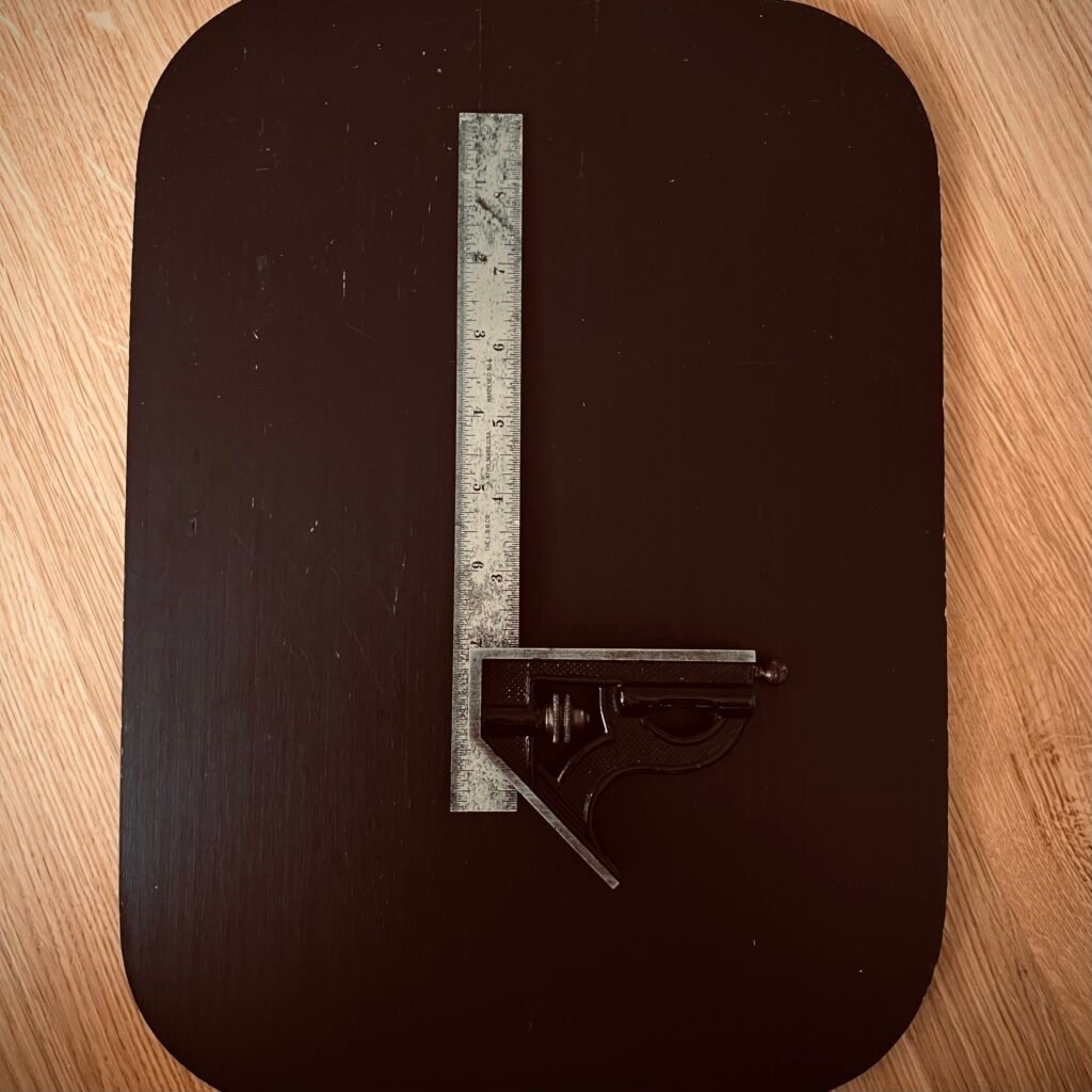 A well-worn combination square resting on a dark wood surface, representing heirloom quality tools built to last a lifetime.