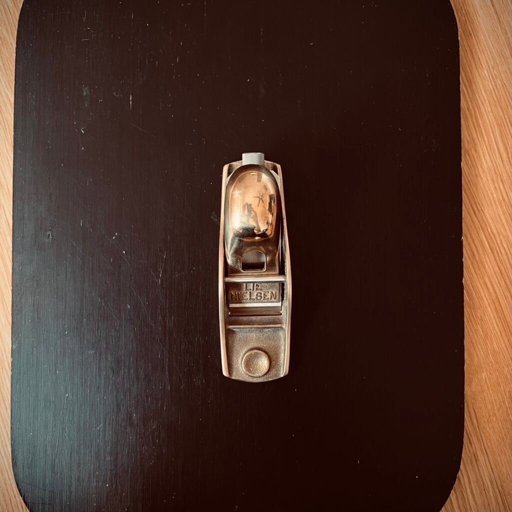 A Lie-Nielsen hand plane resting on a dark wood surface, representing heirloom quality woodworking tools built for precision and a lifetime of use.