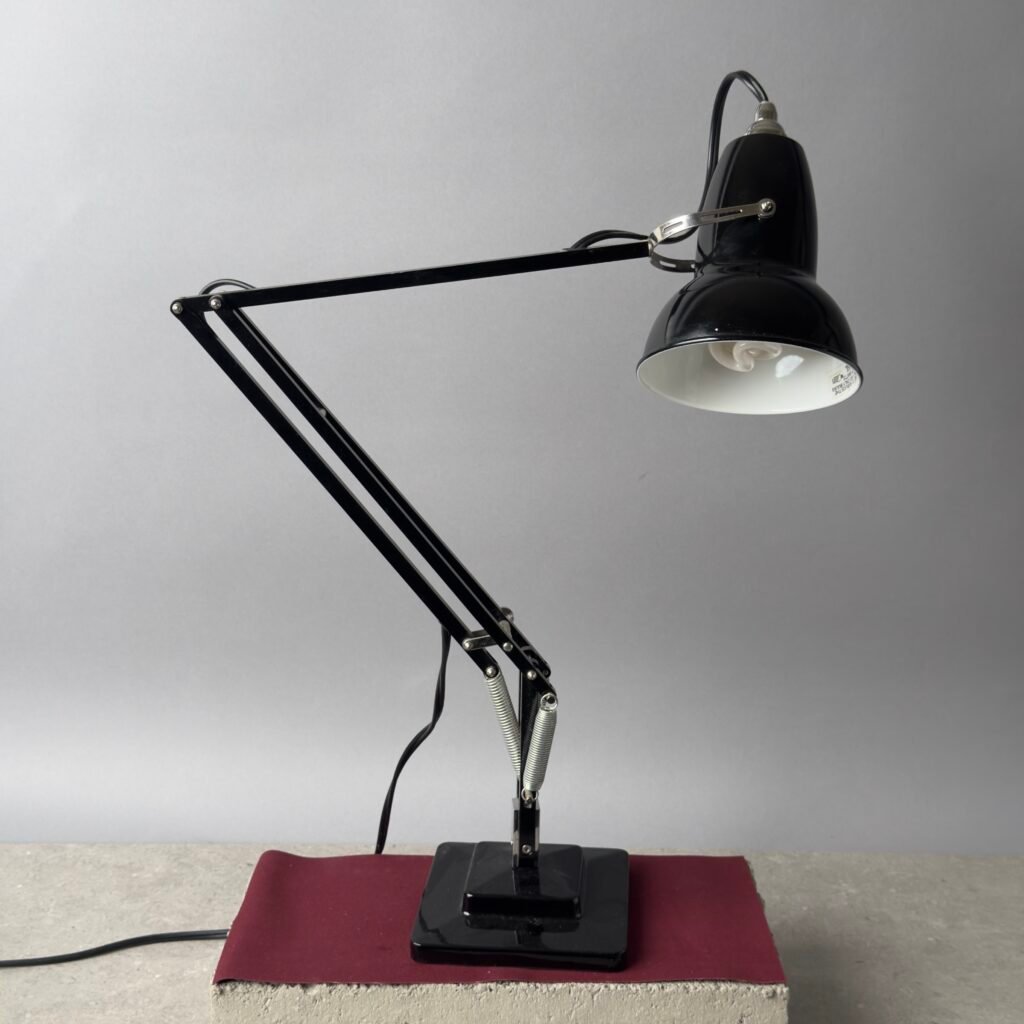 Black Anglepoise desk lamp with adjustable arm on a concrete block against a neutral background