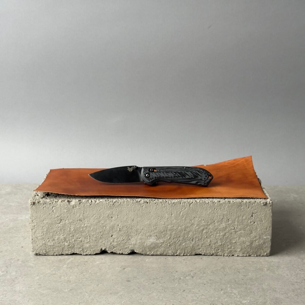 Benchmade Super Freek 560BK-1 black folding knife on a black surface over a concrete block background