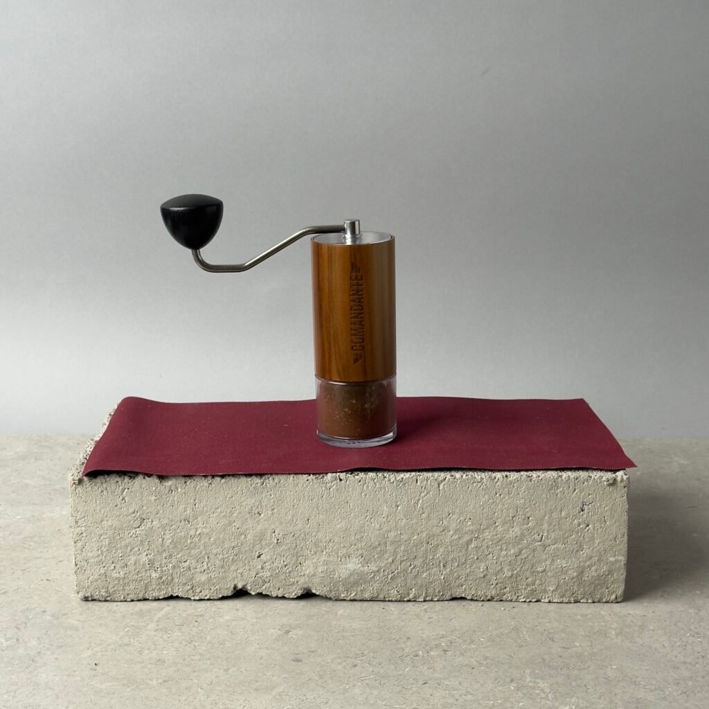 Comandante C40 hand coffee grinder with wooden body and crank handle on a concrete block background