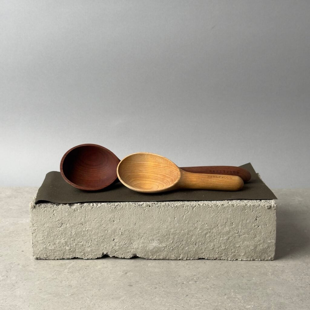 Two Earlywood wooden serving spoons on a concrete block with a neutral background