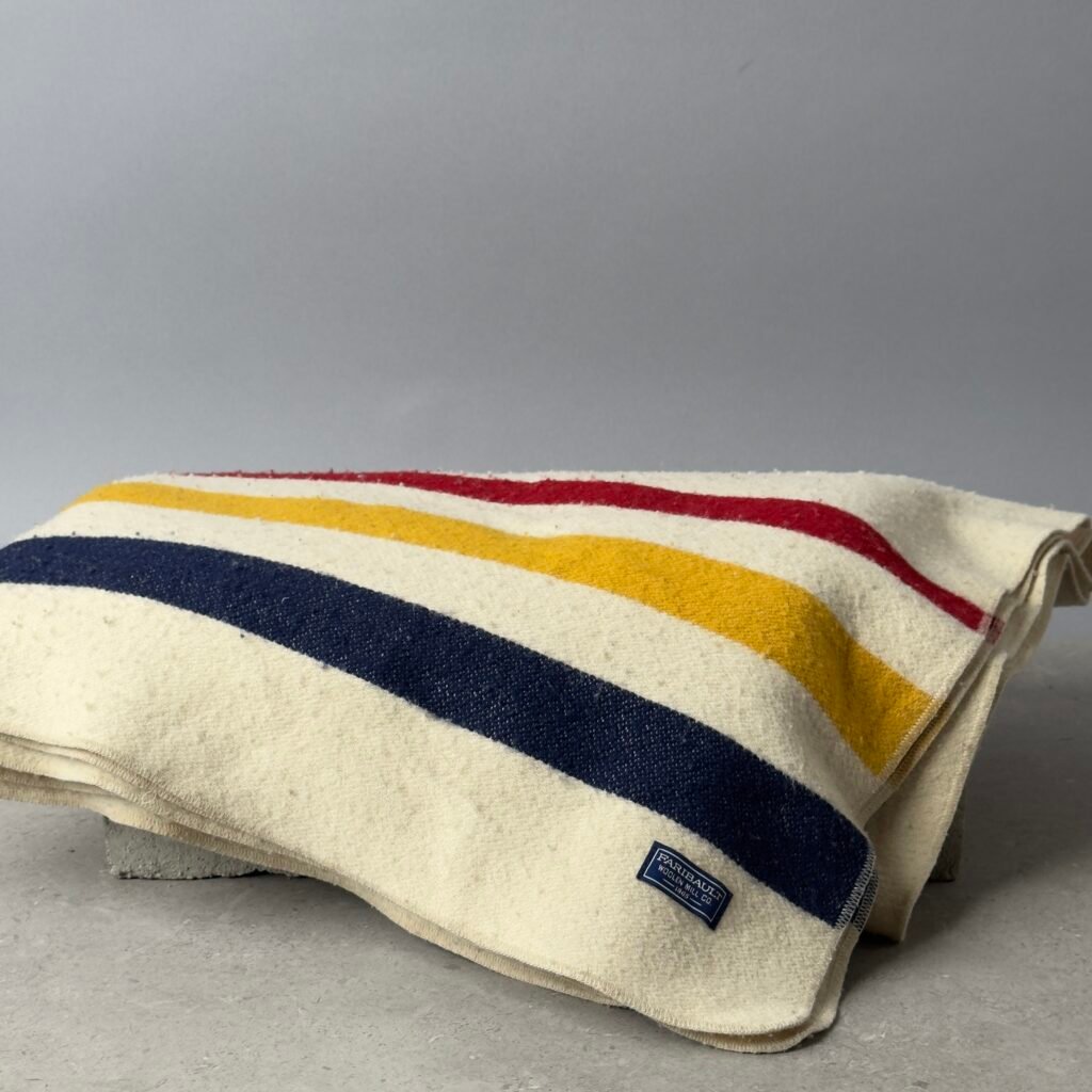Faribault Mill wool blanket with red yellow and navy stripes folded on a neutral studio surface