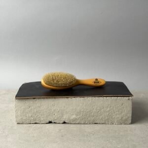 Kent LHS9 satinwood boar bristle hairbrush on a black surface over a concrete block background