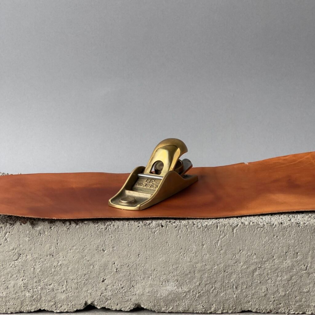 Lie Nielsen No. 102 low angle block plane in bronze on a leather surface against a neutral background