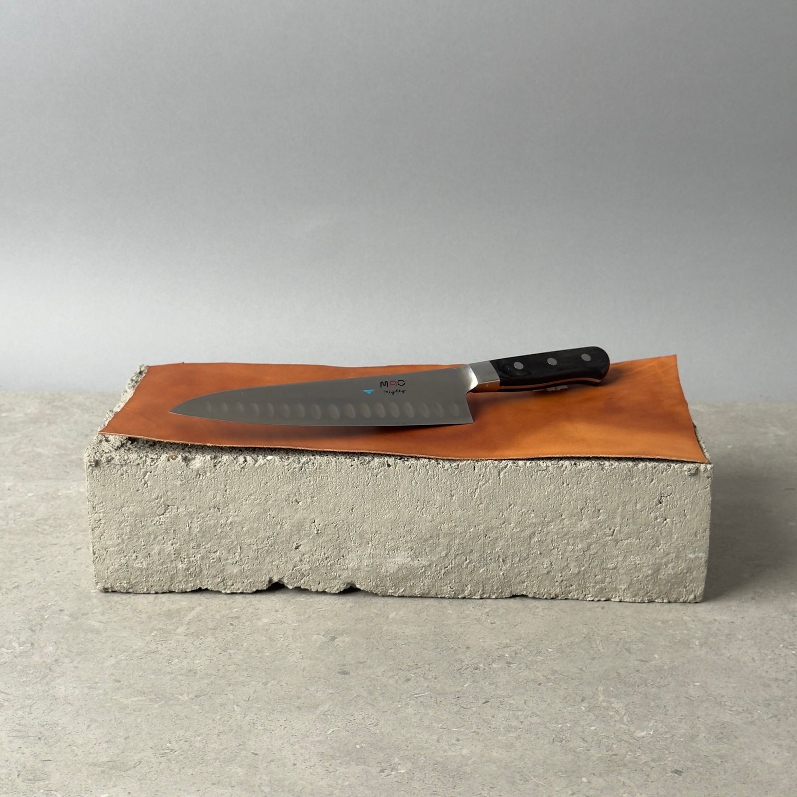 MAC MTH-80 chef knife with granton edge on a leather surface over a concrete block background
