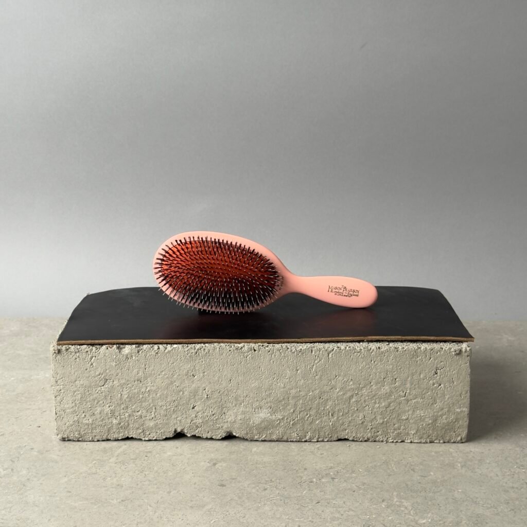 Mason Pearson Popular Brush in pink with bristle and nylon mix on a black surface over a concrete block background