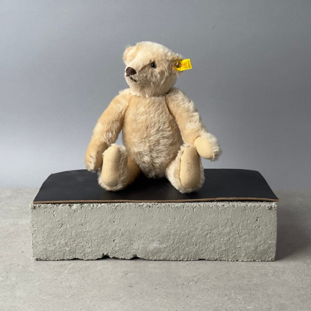 Steiff teddy bear sitting on a concrete block with a neutral background