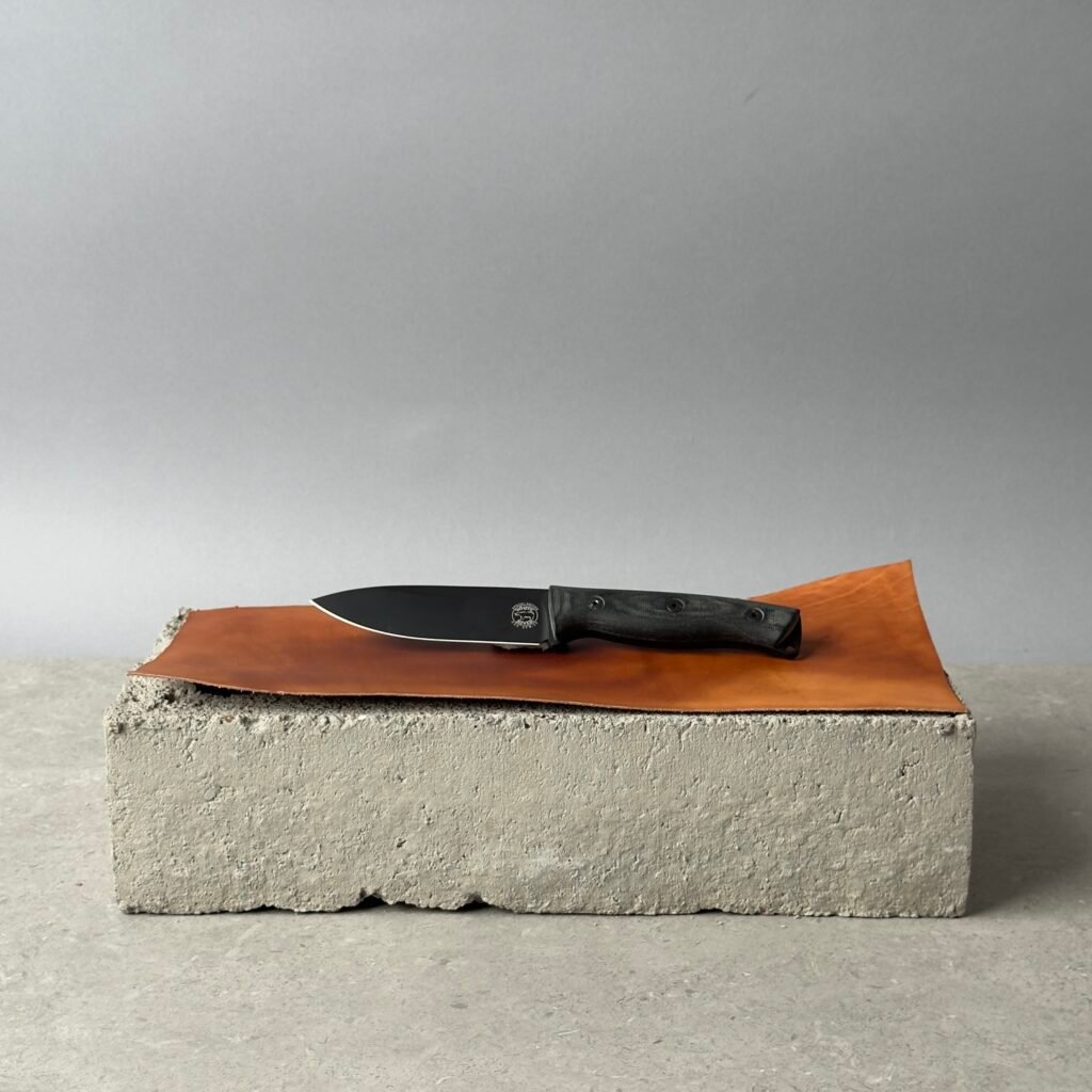 White River Knives Ursus 45 fixed blade knife on a leather surface over a concrete block background