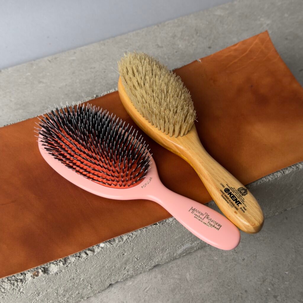 Kent LHS9 satinwood hairbrush and Mason Pearson Popular hairbrush side by side on leather surface